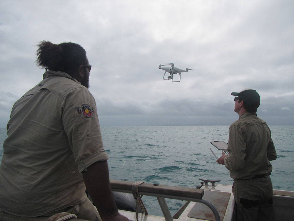 Tom Watson (Droner) and Trevor Nona (NPARC/ Apudthama Ranger) launch the drone from the boat at low tide